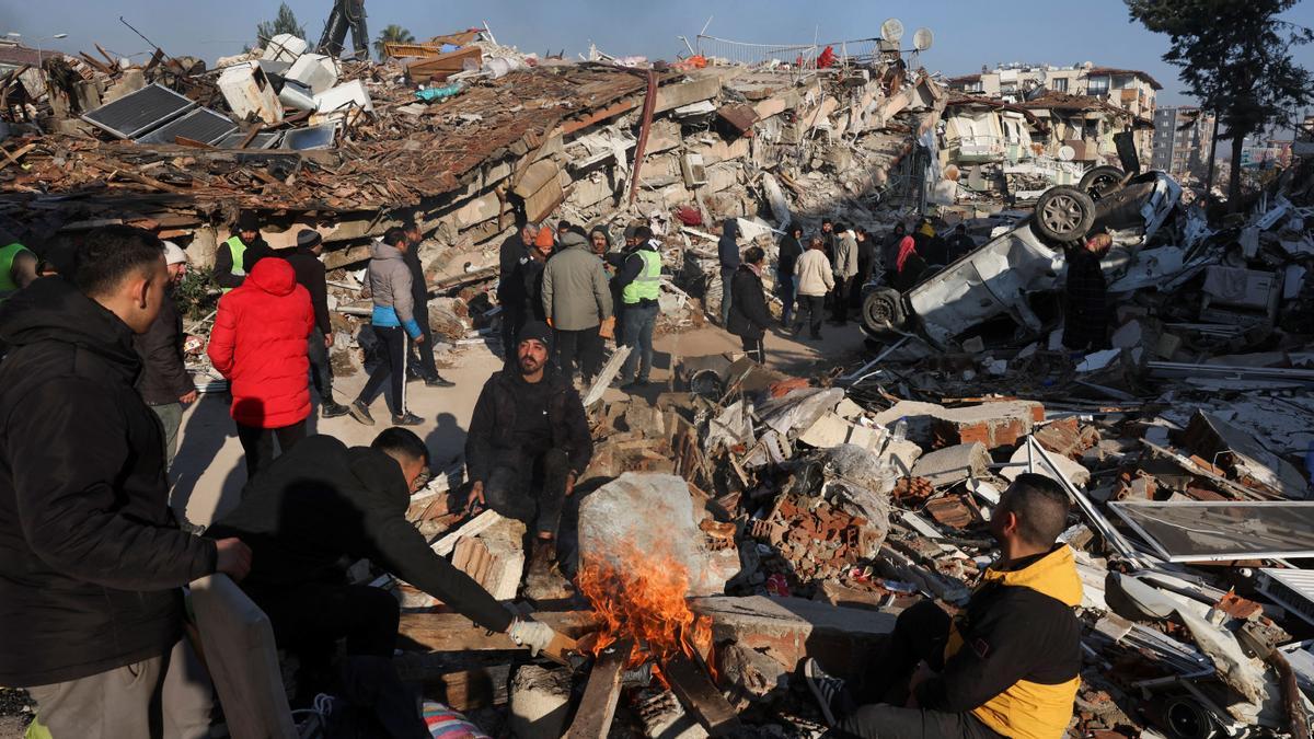 Búsqueda supervivientes, la gente se reúne alrededor de un fuego encendido en medio de los escombros después de un terremoto mortal en Hatay, Turquía