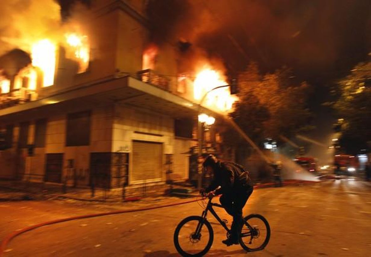 Un ciclista davant d’edificis incendiats a Atenes.
