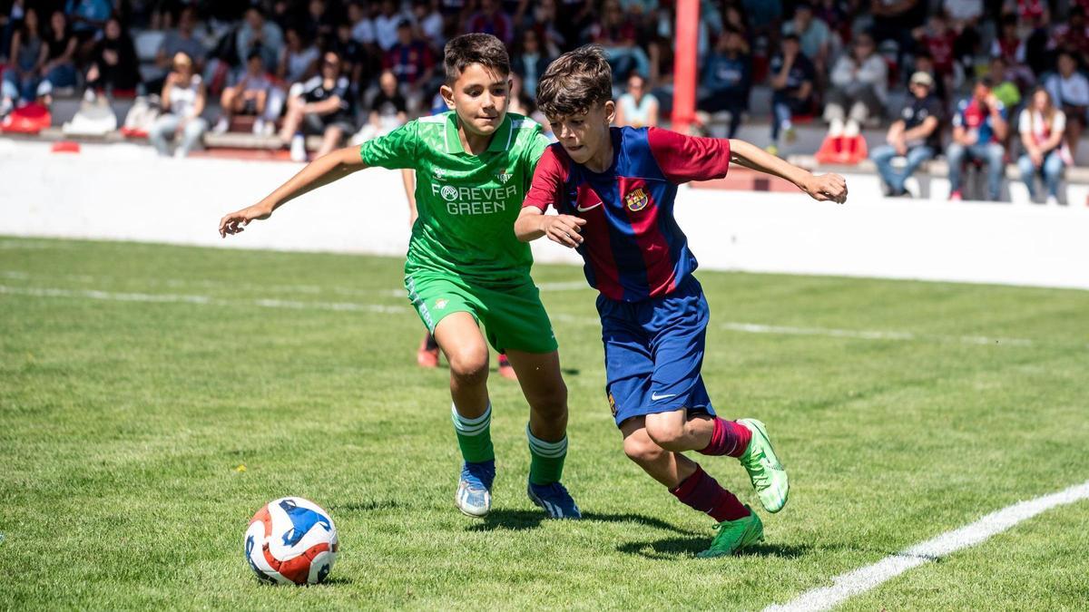 Un jugador del Barcelona conduce el balón perseguido por otro del Betis.