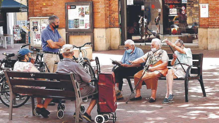 Varias personas mayores, con mascarillas, conversan en el barrio barcelonés de El Clot