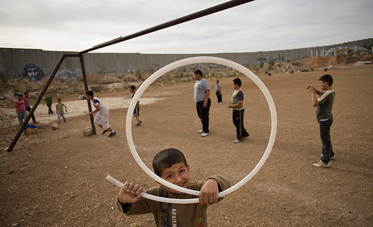 Un nen palestí somriu a la càmera mentre altres juguen, aquest dimecres, a prop del mur instal·lat pel Govern israelià que separa la població cisjordana d’Abu Dis de Jerusalem.