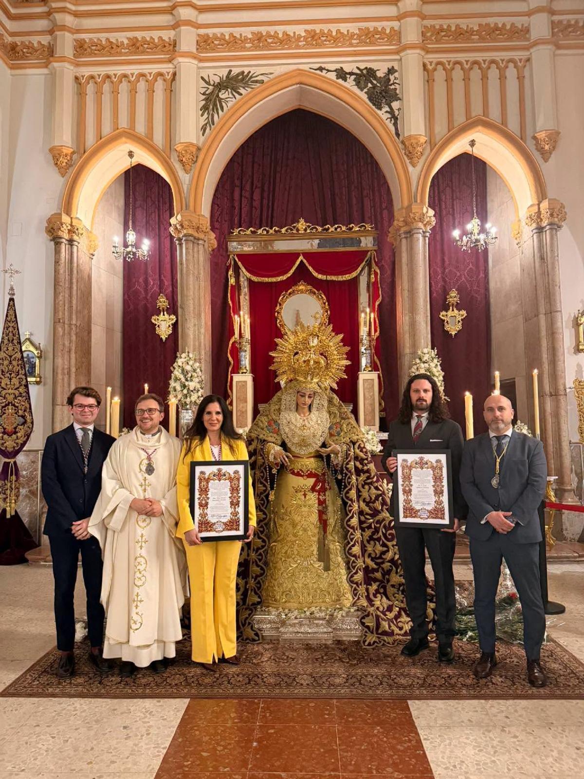 El bordador Miguel Pacheco Pérez, la pregonera del Lunes Santo 2027, Diana Navarro, el pintor del cartel del Lunes Santo, Martín España, y el hermano mayor del Cautivo, Benjamín Palencia, junto a la Virgen de la Trinidad Coronada.