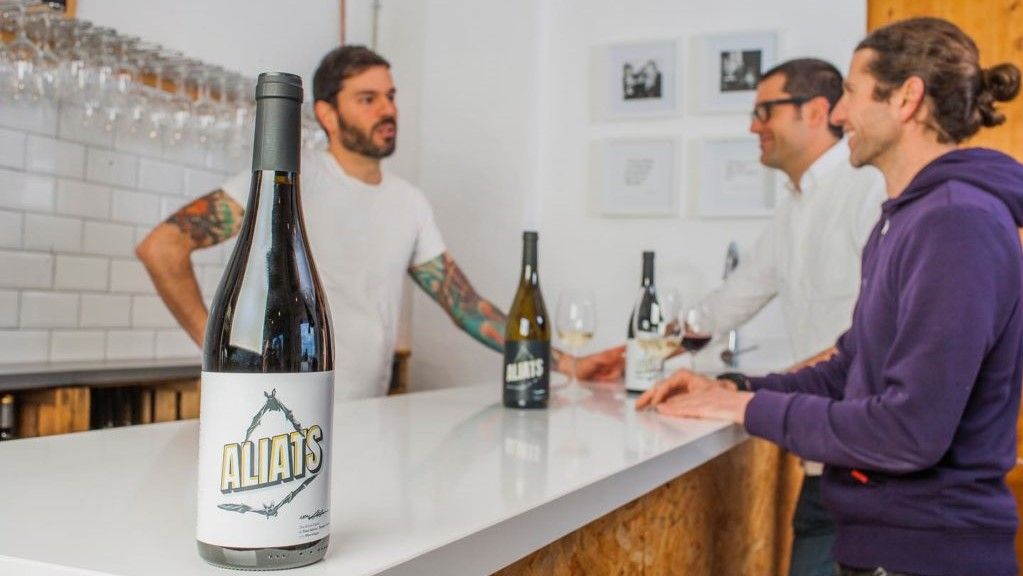 Botellas de Aliats cuyas etiquetas han diseñado ilustradores de Batman por encargo de la tercera generación de Bodegas Enguera (en la foto, al fondo, Pedro, Juan Ramón y Silver).