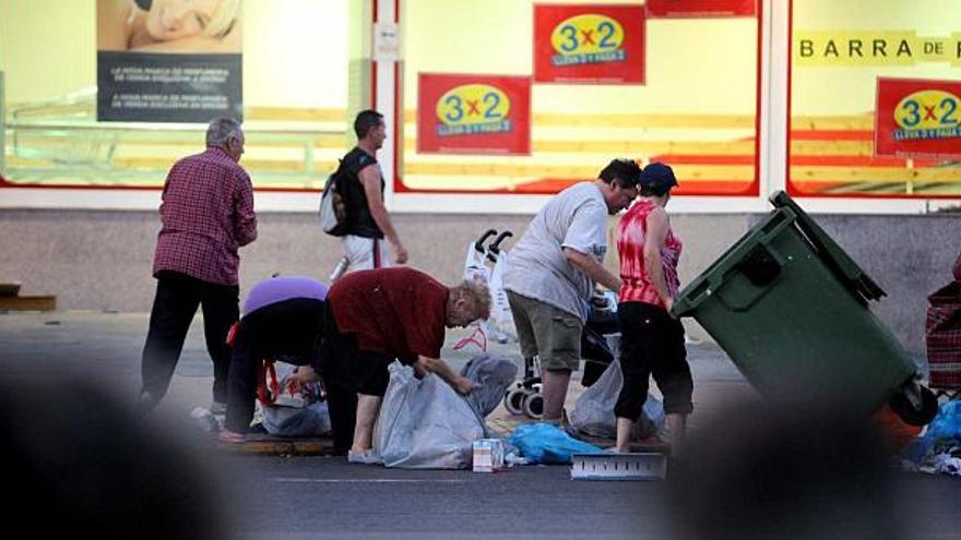 Vecinos de Benidorm sin recursos recogiendo alimentos de los contenedores de un supermercado de la ciudad, ayer por la noche.