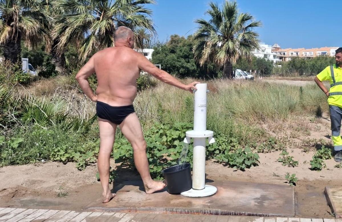 Un bañista llena un cubo con agua potable de los lavapiés de la playa del Raset