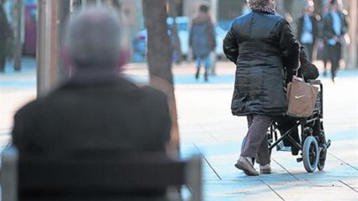 Una mujer pasea a su marido en silla de ruedas, en Barcelona.