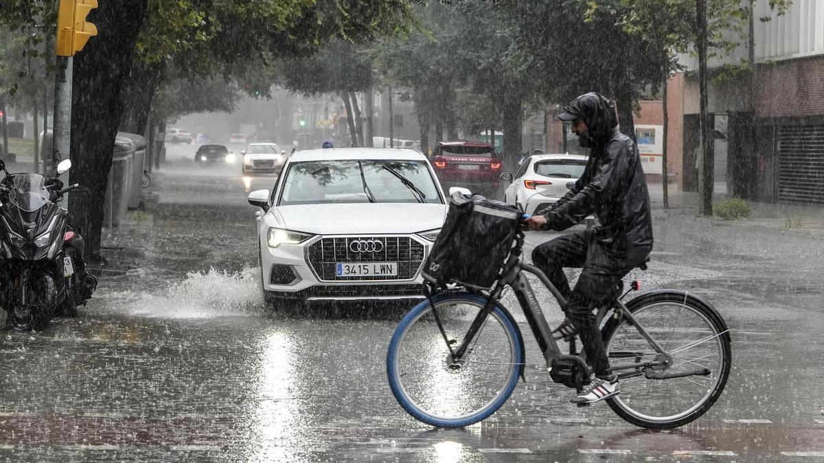 Coches, bicicletas y peatones sortean grandes charcos de agua acumulada en la calle Perú durante la tormenta de lluvia