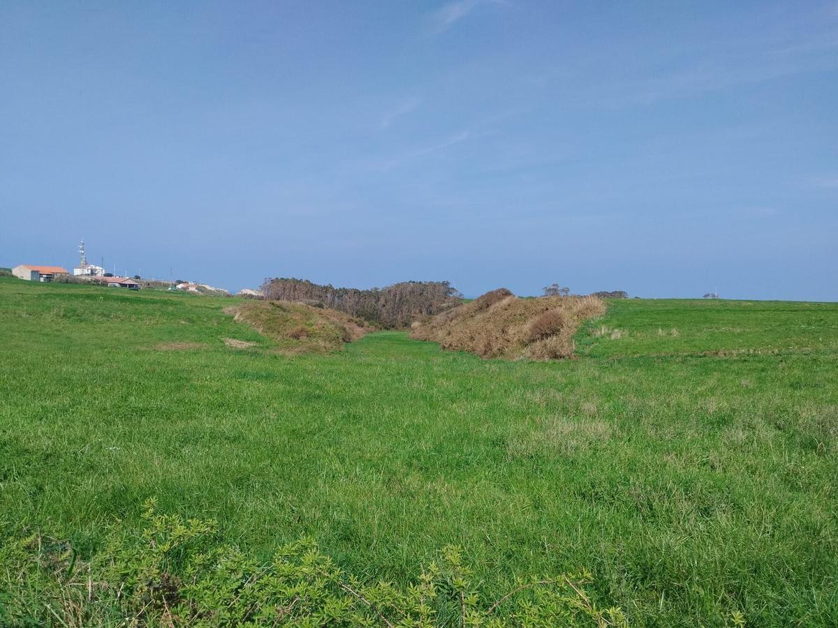 Terrenos en los que se prevé ubicar el nuevo estacionamiento, con el faro de Peñas al fondo