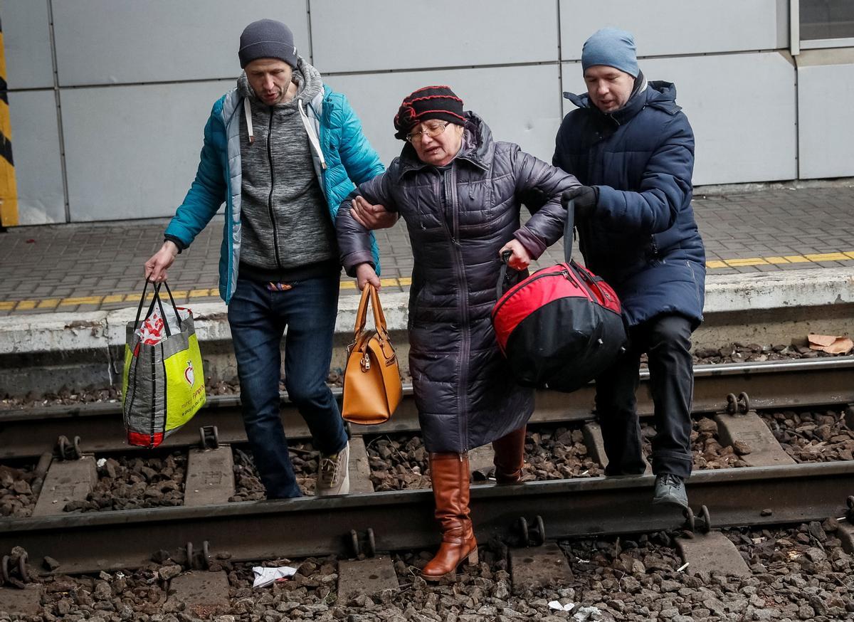 Dos hombres ayudan a una mujer a cruzar la vía para tomar un tren en la estación central de Kiev que la lleve a Leópolis.