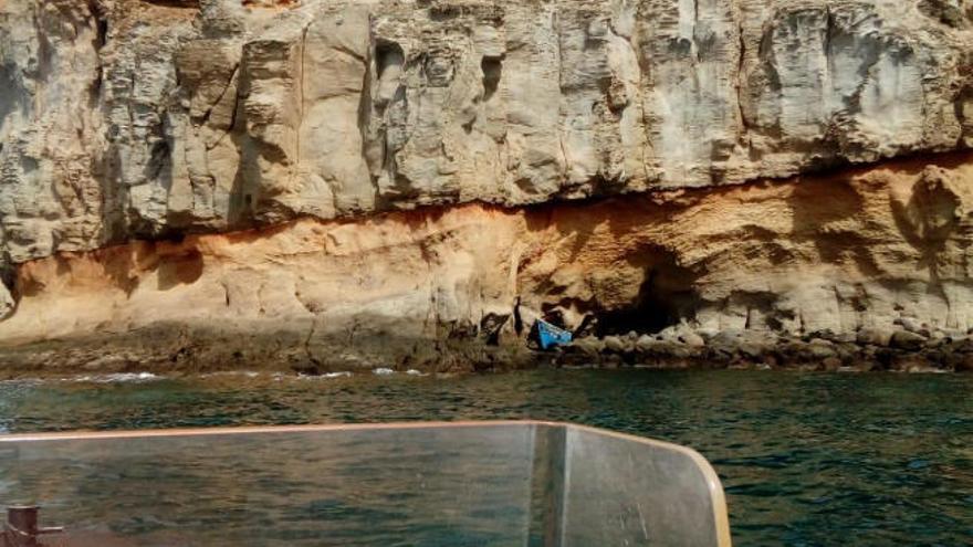 La patera -azul, en el centro-, localizada en un barranco de difícil acceso, ayer, cerca de la playa de Mogán.