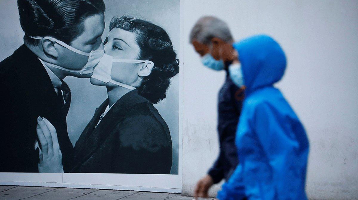 Dos transeúntes pasan junto al cartel de un beso entre dos personas con mascarilla, el domingo 10 de mayo.