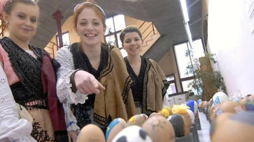 Unas jóvenes vestidas con el traje asturiano señalan los huevos que se muestran en la Casa de Cultura.