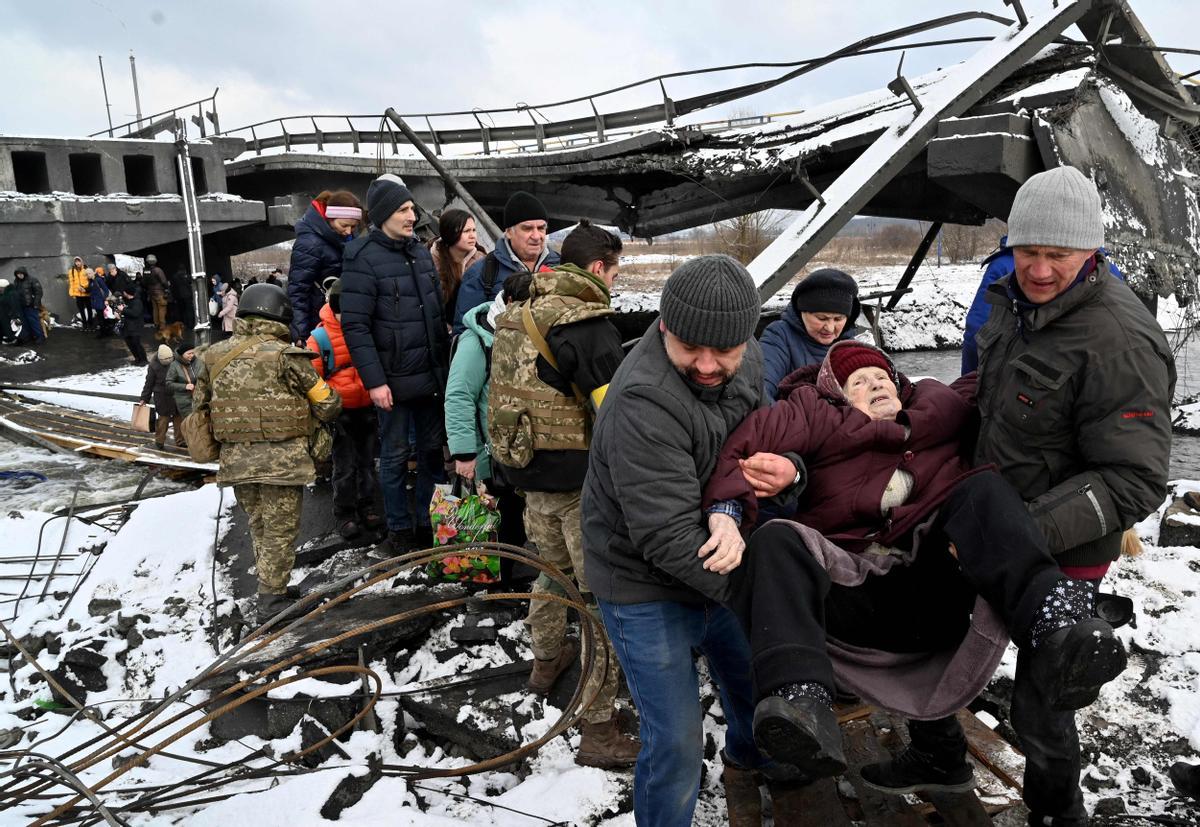 Soldados ucranianos ayudan a una anciana a cruzar un puente destruido en la ciudad de Irpin, al noroeste de Kiev