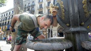 Un turista italiano se refresca con agua de la fuente de Canaletas, en Barcelona.