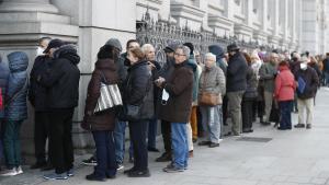 Numerosas personas hacen cola ante el Banco de España para comprar deuda pública.