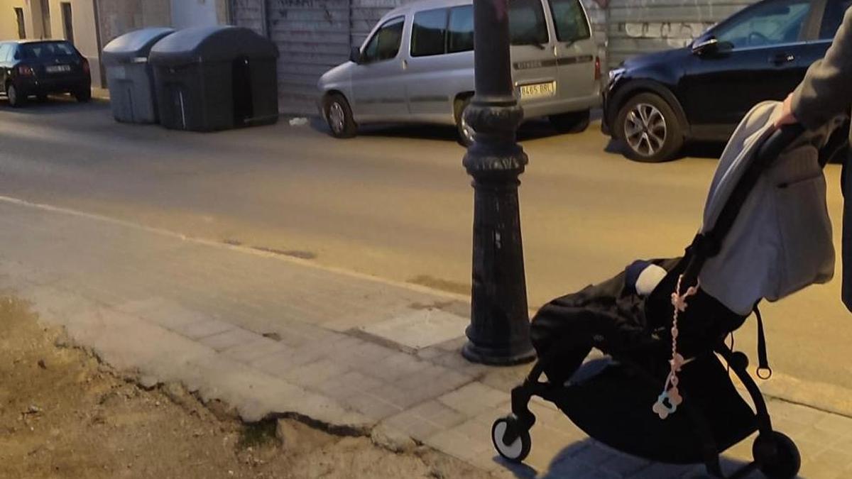 La farola que piden retirar y un carrito pasando por la acera con el adoquin desgastado .