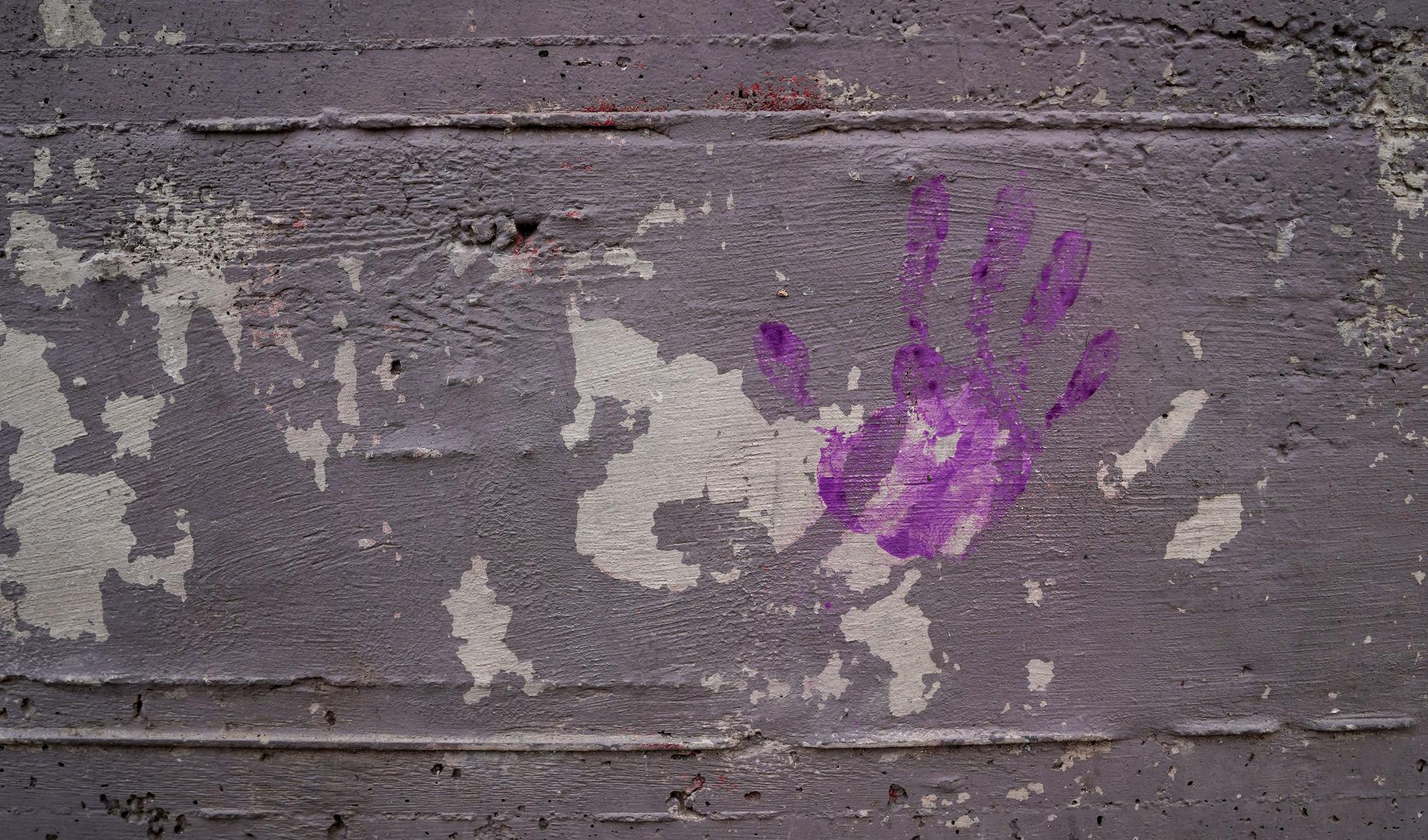 Una mano morada sobre una pared como forma de reivindicar el feminismo en los barrios.