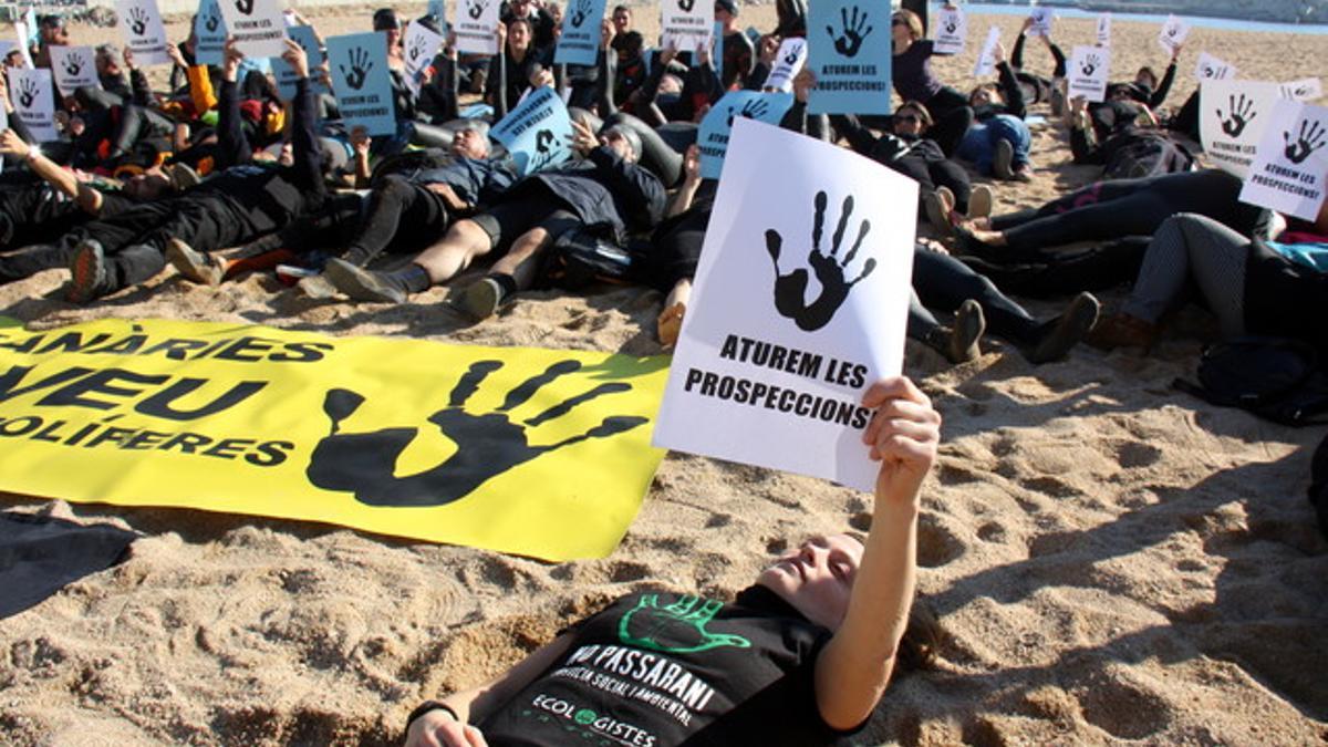 Activistas y nadadores, vestidos de negro, simulan un vertido de petróleo sobre la arena de la playa, este domingo.