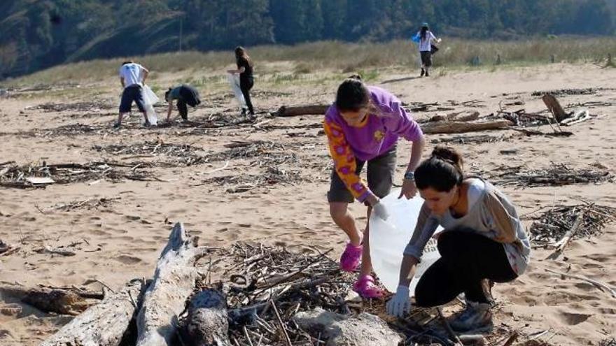 Dos jóvenes recogen plásticos en la playa de Rodiles.