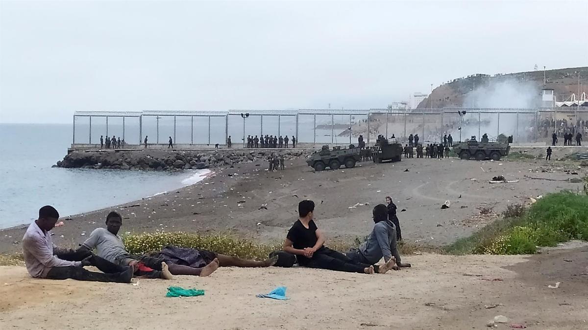 Un grupo de inmigrantes marroquí observa el despliegue del Ejército de Tierra en uno de los espigones fronterizos de Ceuta.