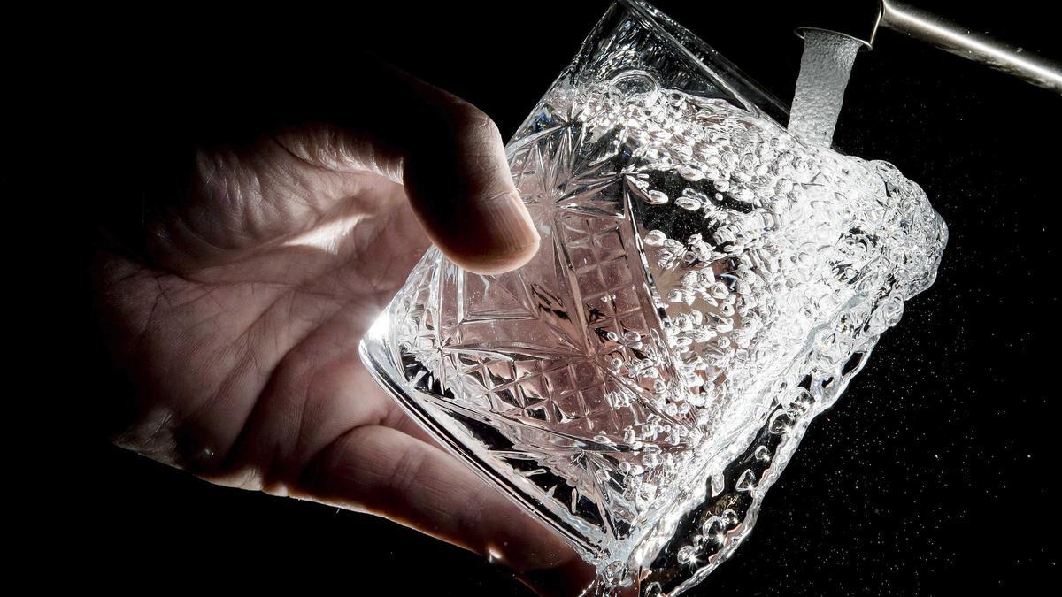 Una persona llenando un vaso de agua en un grifo.