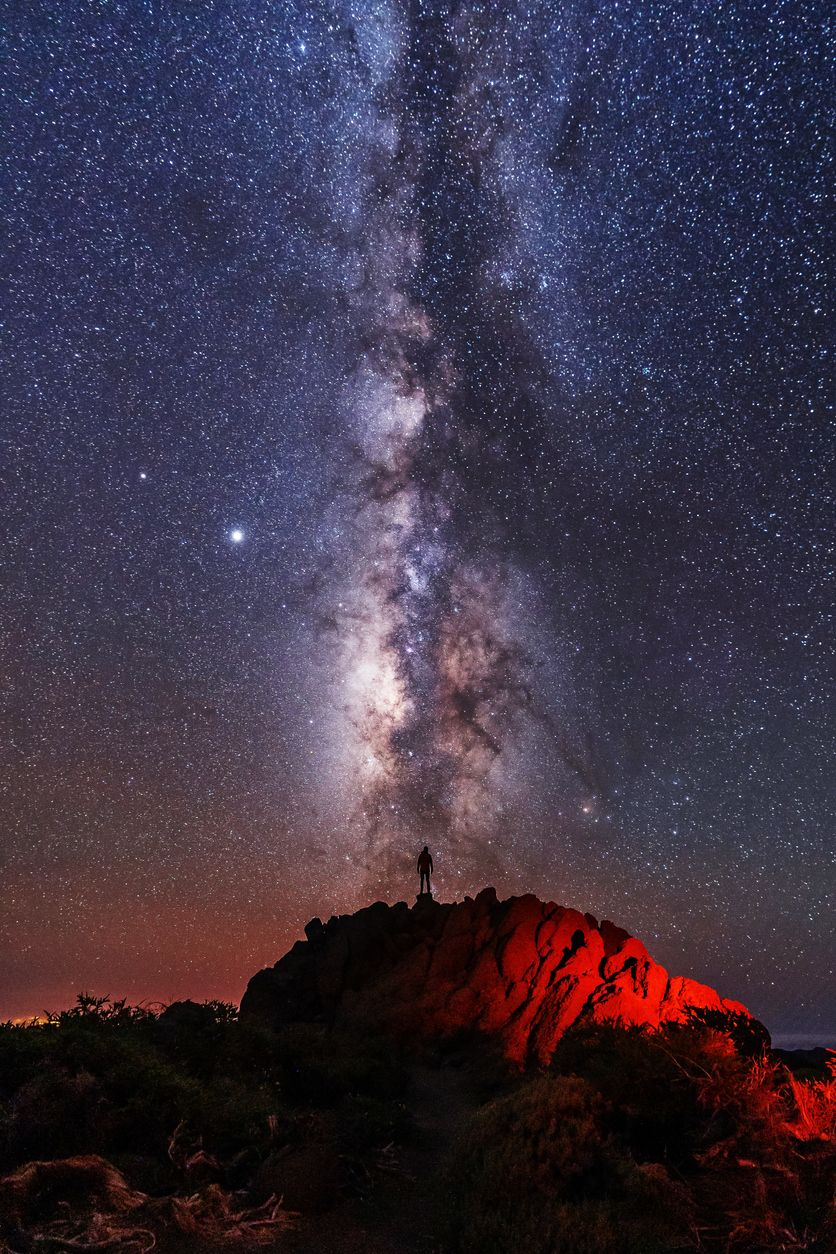 Silueta de un joven bajo las estrellas mirando el camino lactea de la Caldera de Taburiente cerca del Roque de los Muchahos en la isla de La Palma.
