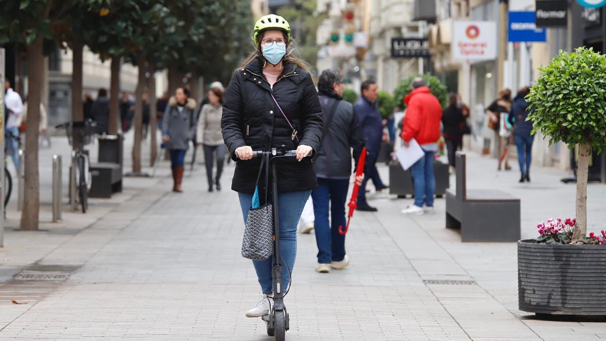 Una joven con mascarilla y en patinete en la calle Cruz Conde de Córdoba.