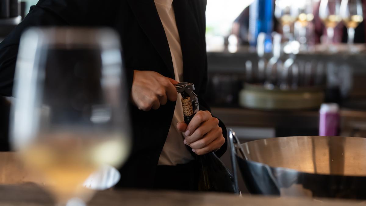 Un camarero abre una botella de vino.