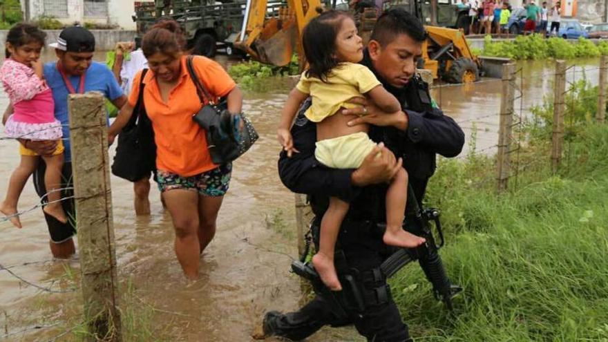 Un policía ayuda a una niña a sortear una zona anegada. efe