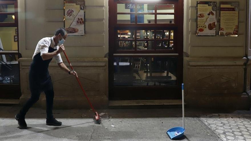 Un trabajador barre el exterior de su bar, en el Centro de Málaga.