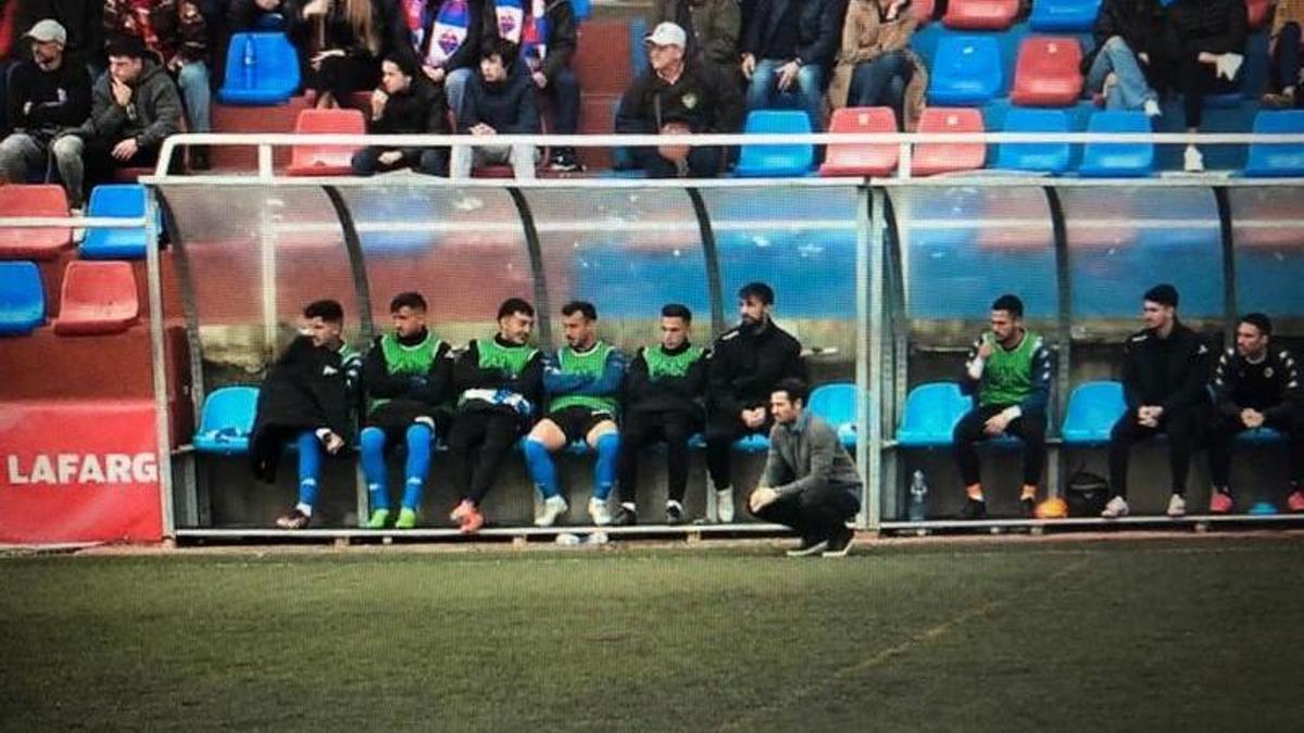 Lolo Escobar observa el partido de cuclillas delante de sus suplentes en el banquillo de Morvedre.