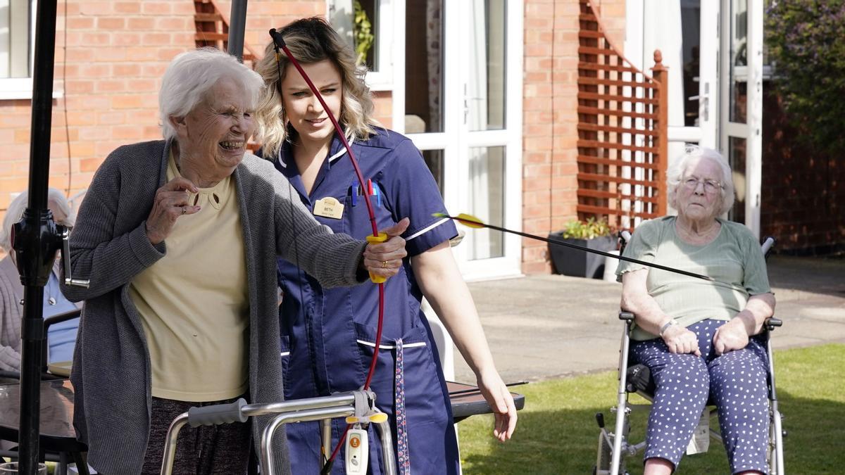 Una trabajadora de una residencia de Leicester observa a una anciana mientras lanza un arco.