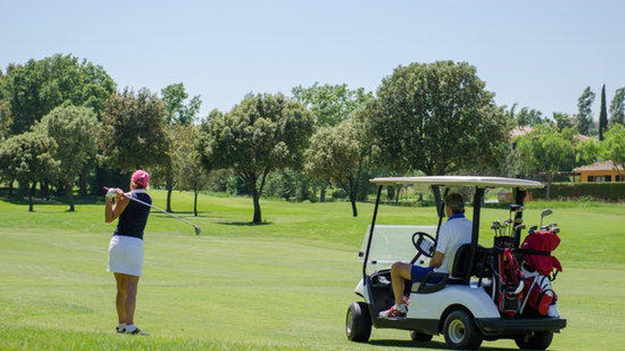 Una jugadora de golf llançant una bola mentre un altre s&#039;ho mira des del carret en el golf de Torremirona en una imatge d&#039;arxiu