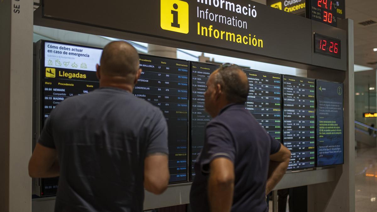 Varias personas observan un panel de llegadas en el aeropuerto.