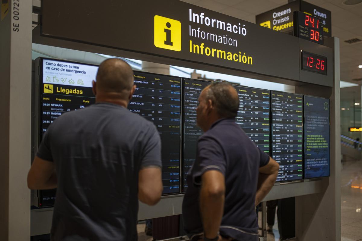 Archivo - Varias personas observan un panel de llegadas en el aeropuerto