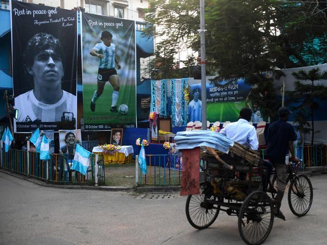 Un hombre monta un carrito de bicicleta frente a las fotos gigantes de la leyenda del fútbol argentino Diego Armando Maradona instaladas en el local de un club en Calcuta.