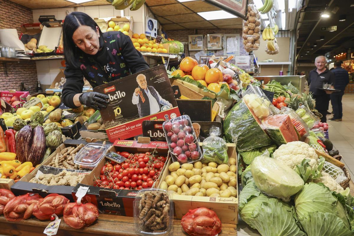 Una mujer coloca un cartel en su puesto de frutas y verduras en Alicante.