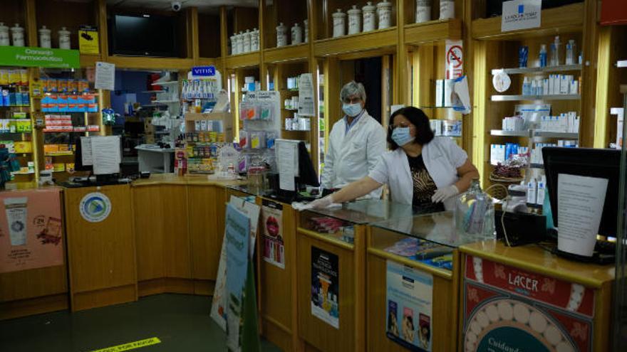 El personal de la farmacia de Rogelio Tenorio Hernández, con Epis, mientras desinfectan el mostrador del establecimiento.