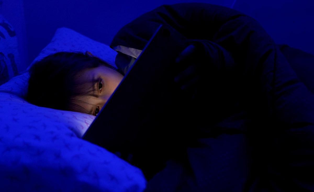 Una menor de edad sujeta una tablet en la cama.