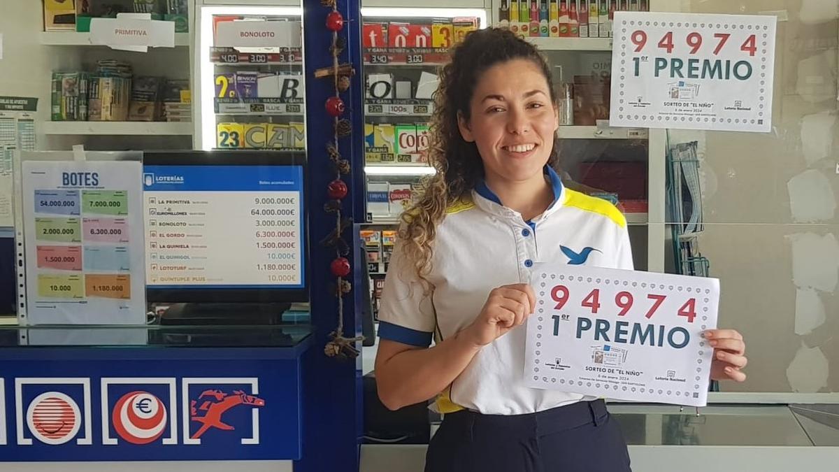 Claudia Lucero, muestra el cartel del primer premio de la Lotería del Niño 2024, vendido en parte en la gasolinera de Mozaga.