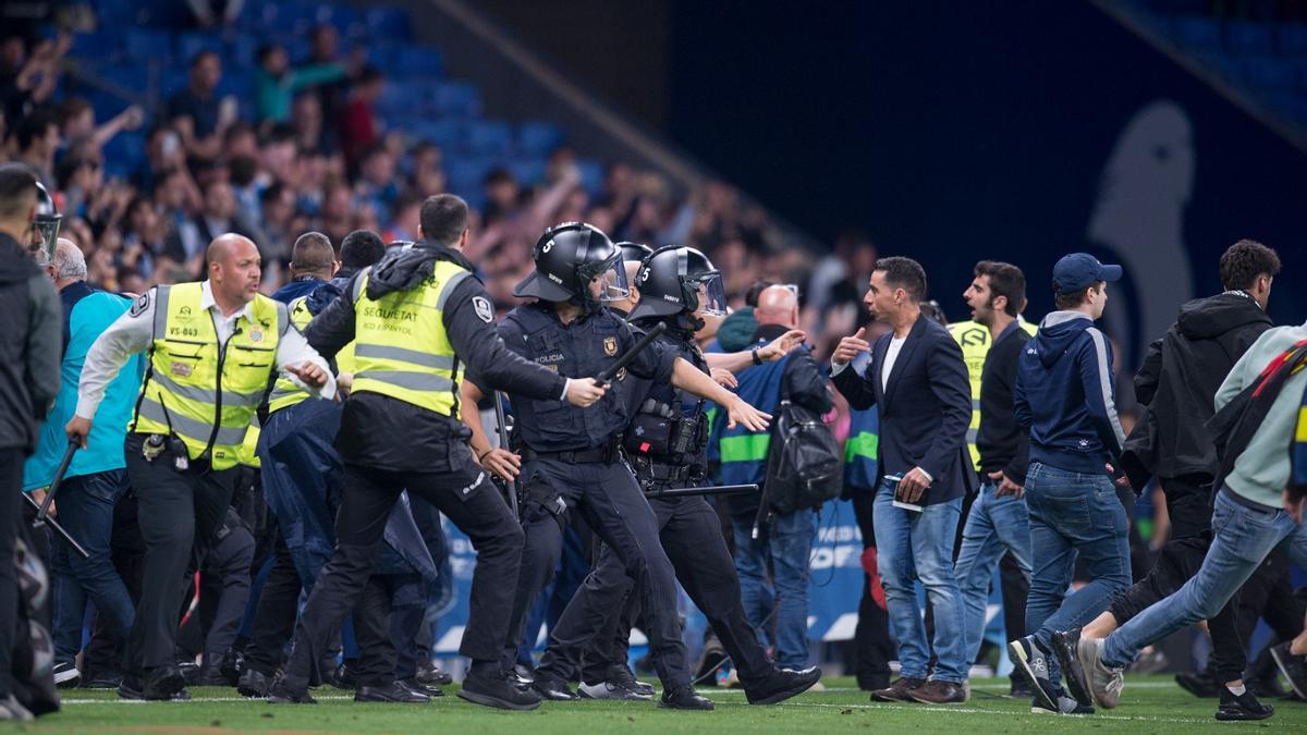 Los miembros de seguridad y los Mossos D'Esquadra frenan a los aficionados radicales que invadieron el campo.