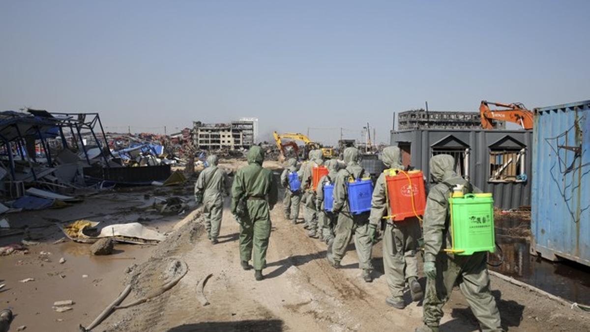 PLA soldiers of the anti-chemical warfare corps in protection suits walk among the debris at the site of last week's blasts in Binhai new district of Tianjin