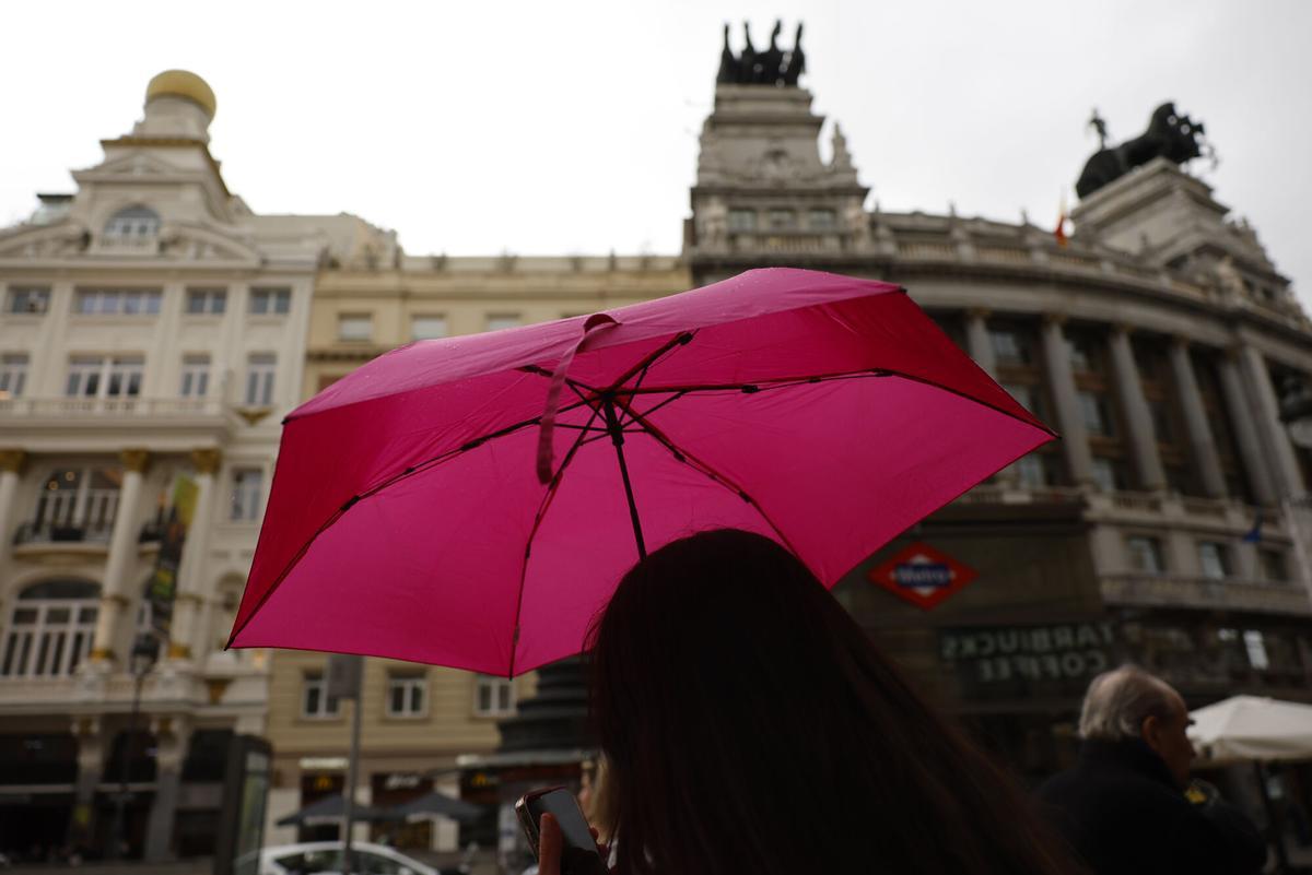 Viandantes se protegen de la lluvia con paraguas por el centro de Madrid.