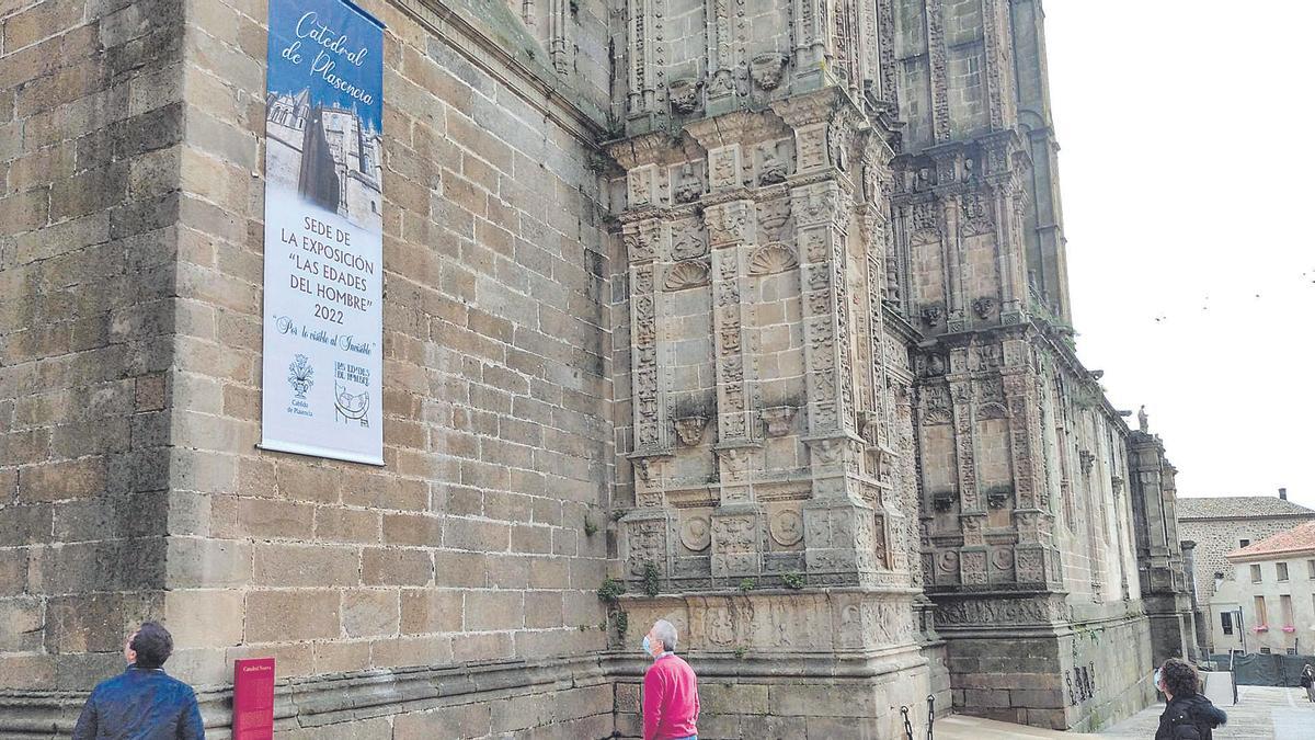 Varios transeúntes contemplan el cartel de Las Edades del Hombre instalado en la catedral de Plasencia.