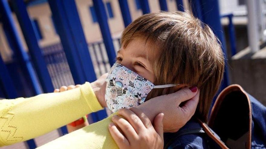 Una madre pone a su hijo una mascarilla a las puertas de un colegio.