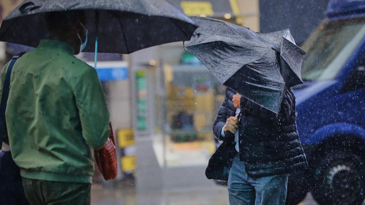 Dos personas se protegen del viento y la lluvia con paraguas.