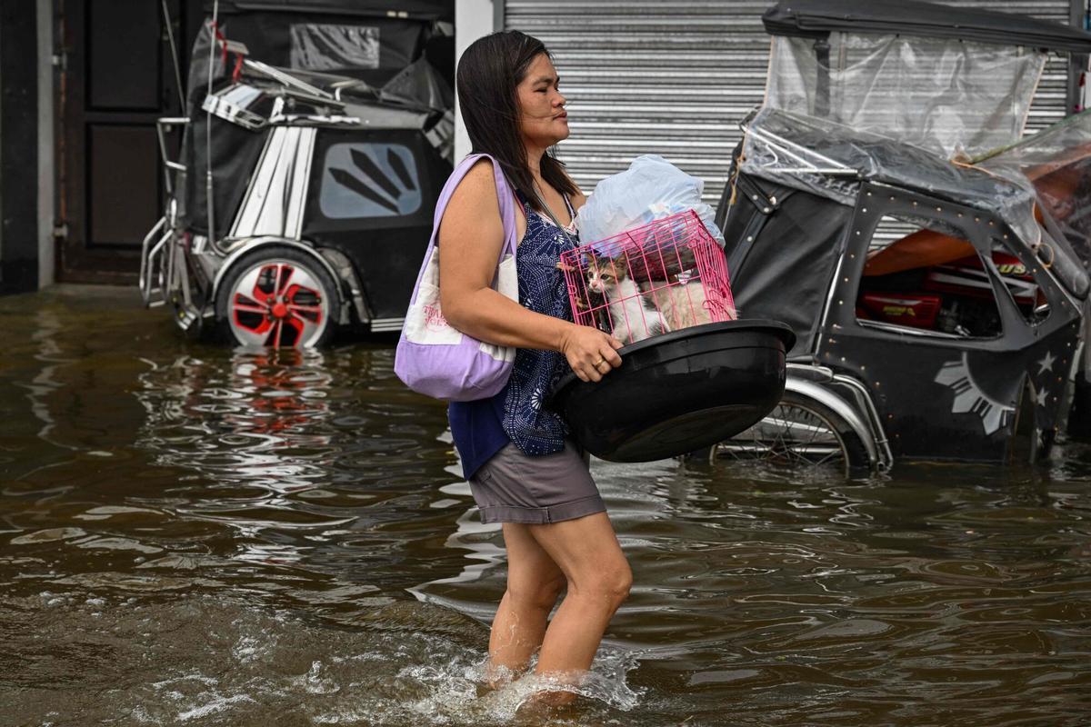 Una mujer que lleva a un gato camina a través de una calle inundada después de las fuertes lluvias traídas por el monzón del suroeste en Pampanga el 31 de agosto de 2026. (Foto de Jam STA ROSA / AFP)