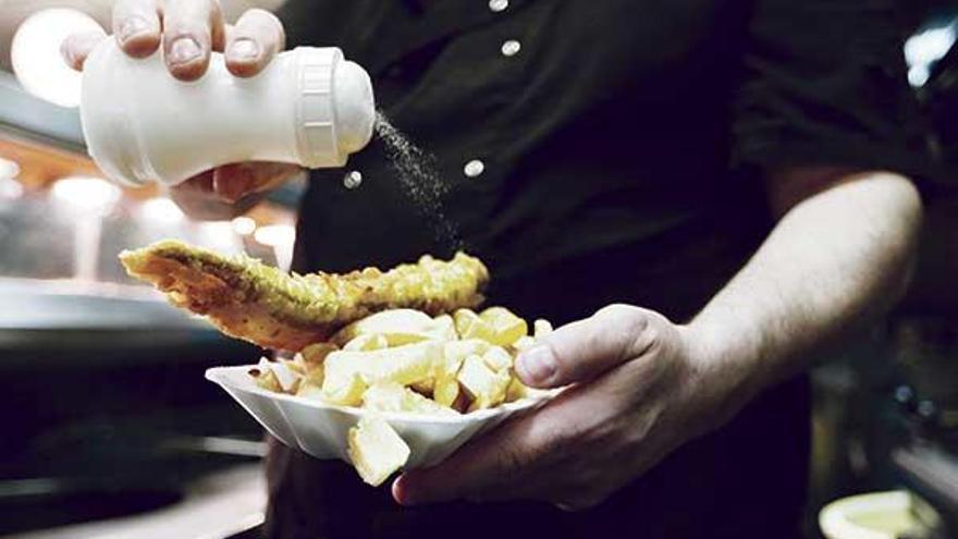 Un hombre condimenta con sal un plato de pescado y patatas fritas.  // Reuters