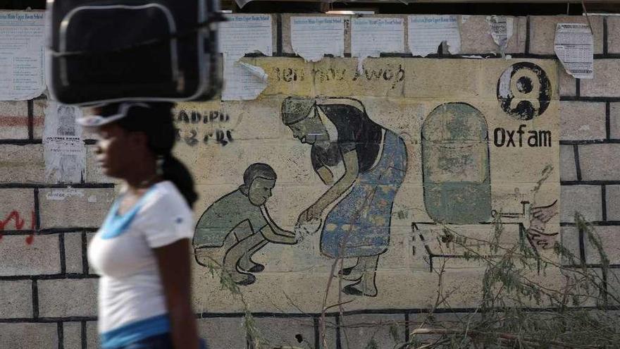 Una mujer camina con una maleta en la cabeza junto a un letrero de Oxfam en Corail, un campamento para personas desplazadas del terremoto de 2010, en las afueras de Puerto Príncipe, Haití. // Reuters