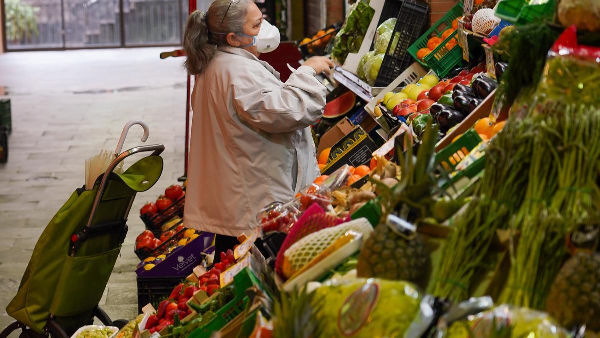 Una señora con mascarilla compra en un mercado.